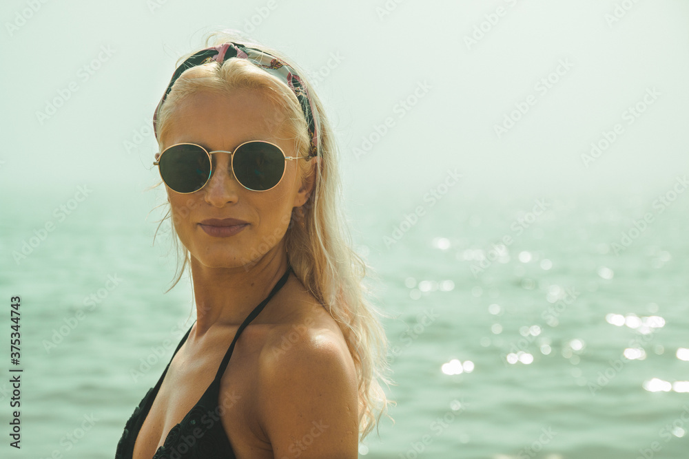 An attractive happy blonde women looking at camera with a smile on a beach with foggy sea in background