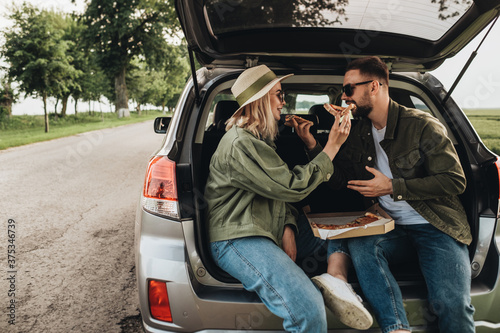 Man and Woman Sitting in the Trunk of Their Car and Eating Pizza © Romvy