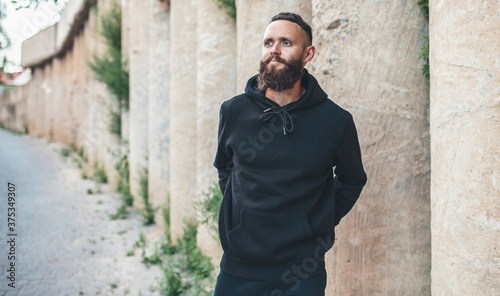 City portrait of handsome hipster guy with beard wearing black blank hoodie or sweatshirt with space for your logo or design. Mockup for print © San4ezz007
