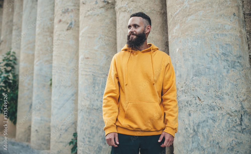 Fototapeta premium City portrait of handsome hipster guy with beard wearing yellow blank hoodie or sweatshirt with space for your logo or design. Mockup for print