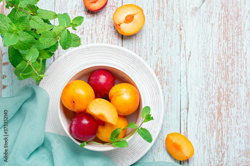 Yellow and red plums in a plate on worn wooden table flat lay, autumn fruits concept, copy space