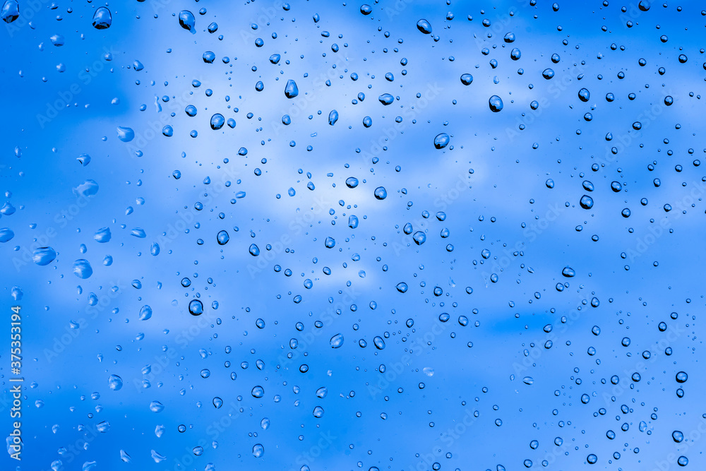 blue rain water drops on a window glass close up with sad clouds in background, drop macro texture ; bad weather backdrop blue rain water drops on a window glass close up with sad clouds in background, drop macro texture ; bad weather backdrop