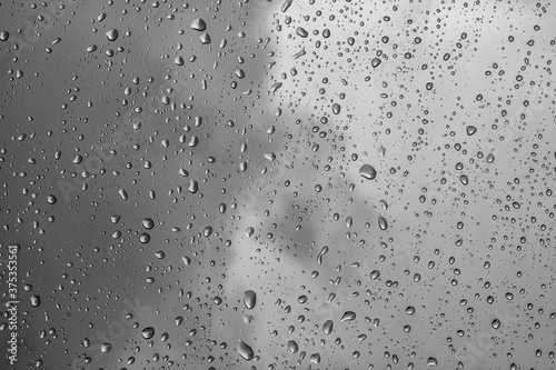 black and white rain water drops on a window glass close up with sad clouds in background, gray drop macro in a golden light ; bad weather backdrop textute