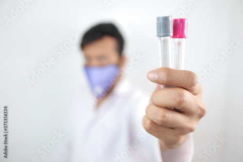 a medical professional in white coat and protective mask holding vials in hand with selective focus in hand with blurred background