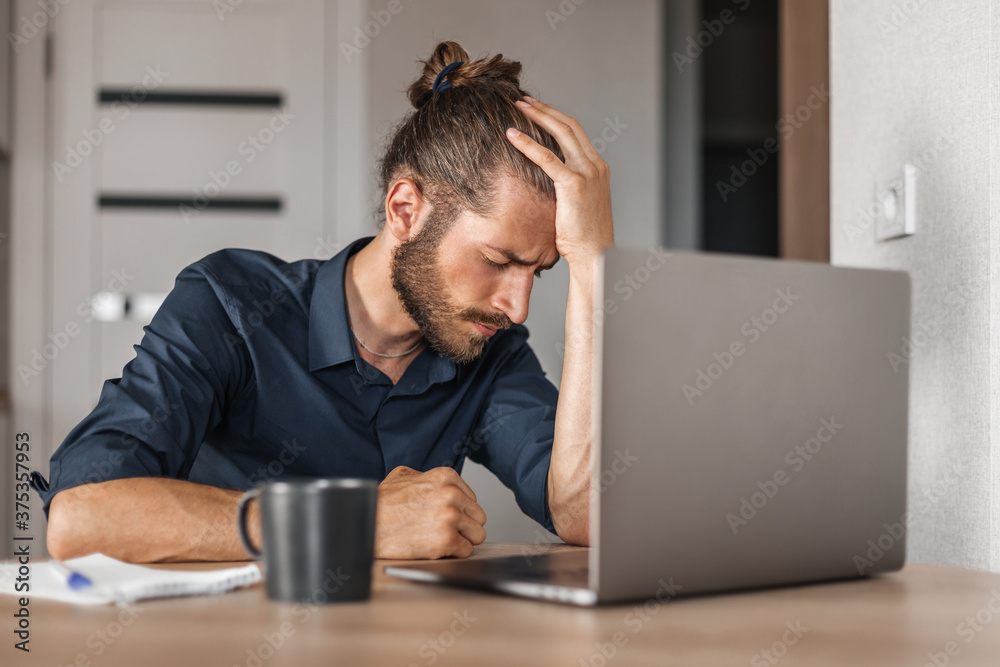 Tired man with headache working at home using laptop Tired man with headache working at home using laptop