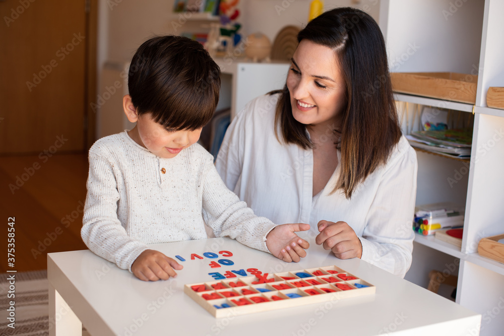 Fototapeta premium Kid learning to write and read with a alphabet and mother or teacher help. Homeshooling. Learning Community. Montessori School