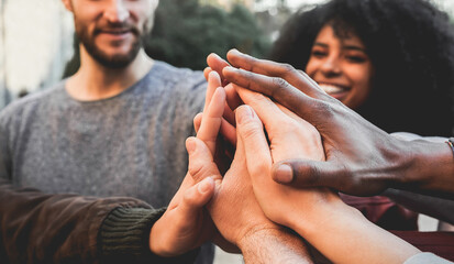 Young happy people stacking hands outdoor - Diverse culture students celebrating together - Focus on hands
