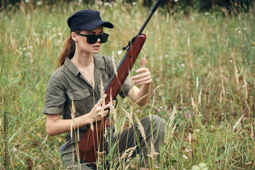 Woman soldier Sitting on the grass weapon in the hands of dark glasses hunting green leaves 