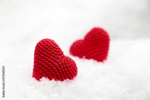 Love hearts, two red knitted symbols of passion in the snow drift, selective focus. Background for Valentine's or Christmas card