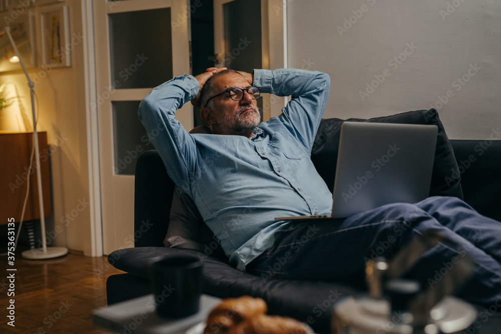 middle aged man sitting sofa and resting using laptop computer at home