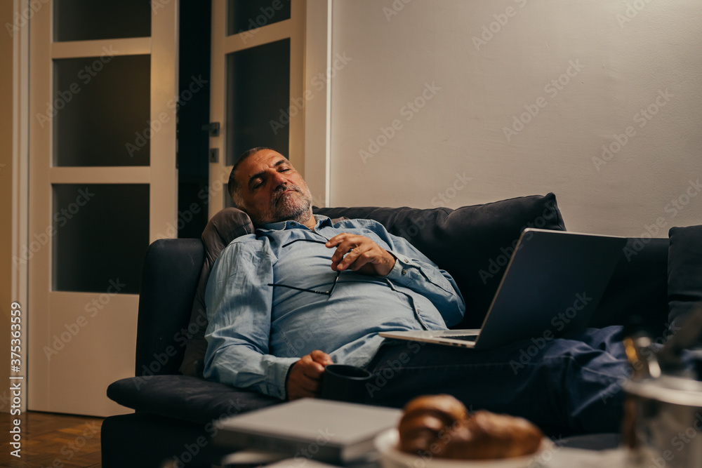 Fototapeta premium middle aged man sitting sofa asleep while using laptop computer at home