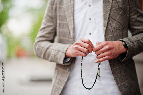 Stylish pakistani man wear in jacket, hold tasbeeh or prayer beads on hand. photo