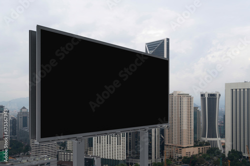 Blank black road billboard with Kuala Lumpur cityscape background at day time. Street advertising poster  mock up  3D rendering. Side view. The concept of marketing communication.