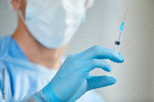 Close-up shot of unrecognizable medical worker wearing protective mask and gloves holding syringe with Covid-19 vaccine
