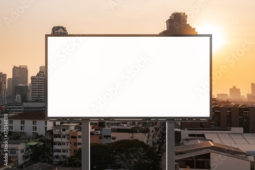 Blank white road billboard with Bangkok cityscape background at sunset. Street advertising poster, mock up, 3D rendering. Front view. The concept of marketing communication to promote or sell idea.