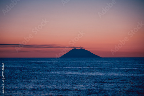 Amazing view of the Stromboli Volcano at sunset  wit the sun going down and amazing sea and sky colors. View form the coast of Calabria  Italy  in the touristic destination of Tropea.
