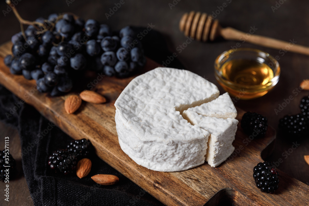 Camembert or brie french soft cheese with grapes, honey, nuts and berries on wooden background. Camembert or brie french soft cheese with grapes, honey, nuts and berries on wooden background.