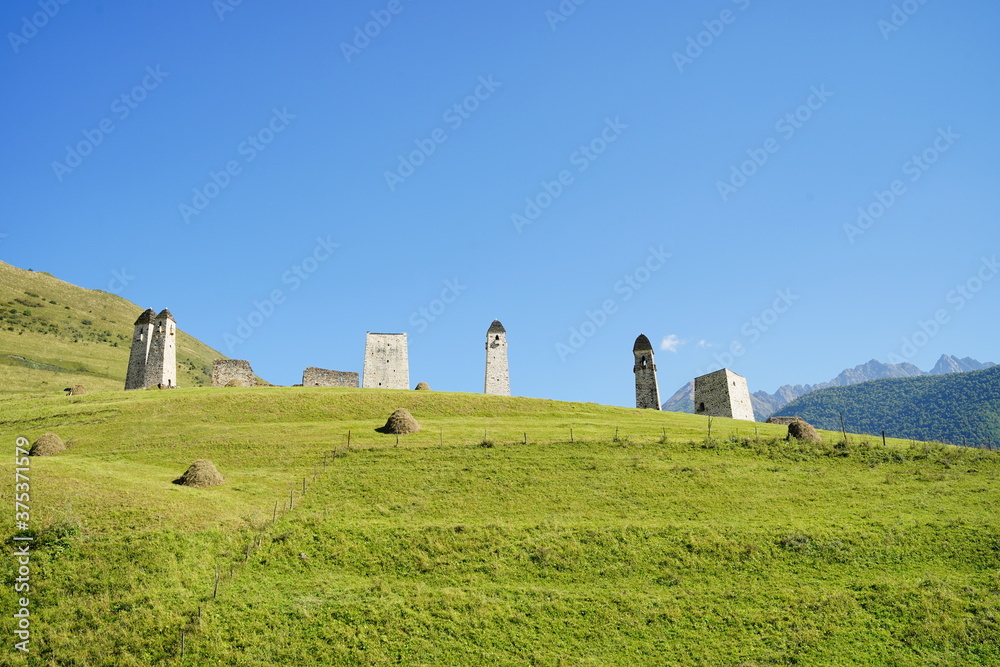 Old stone towers in green mountainous terrain. Ancient stone buildings of old town located on green hill against mountains covered with forest and fog in summer day