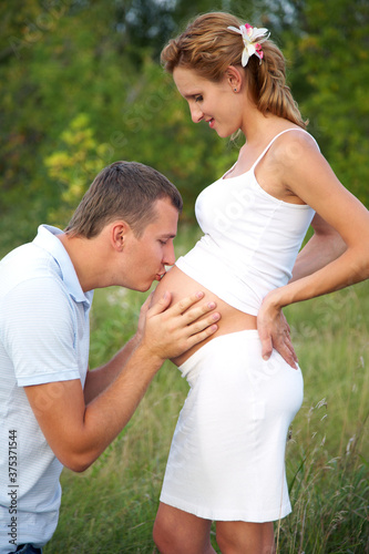 happy pregnant woman and her husband embracing her abdomen