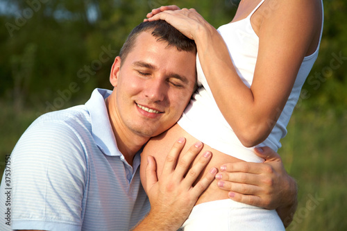 happy pregnant woman and her husband embracing her abdomen