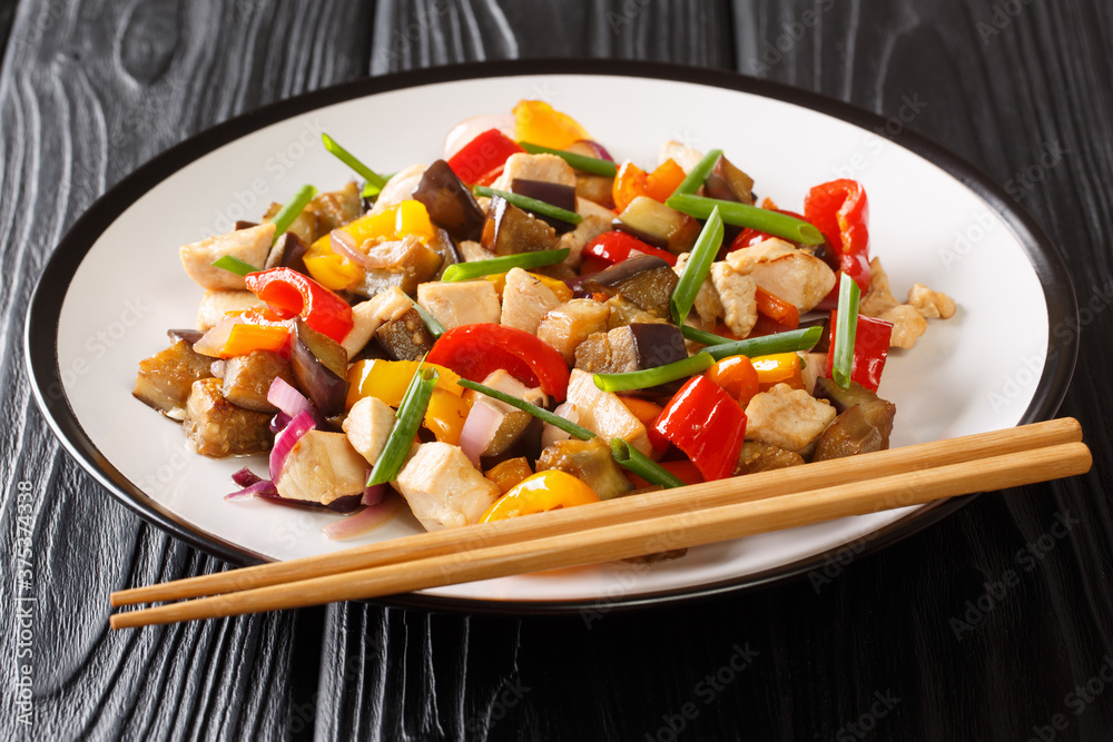Serving of fried chicken and vegetables with eggplant, peppers and onions in a spicy soy sauce close-up in a plate on the table. horizontal Serving of fried chicken and vegetables with eggplant, peppers and onions in a spicy soy sauce close-up in a plate on the table. horizontal