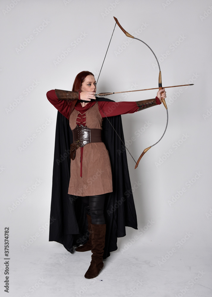 Full length portrait of girl with red wearing medieval archer costume with black Standing
