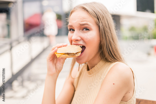 Portrait of beautiful woman eating tasty hamburger at the street cafe. Beauty woman in cafe eating hamburger