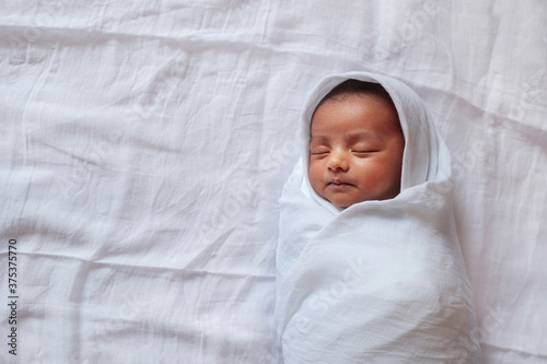 a one month old baby sleeping and swaddled in white cloth lying in white cloth background