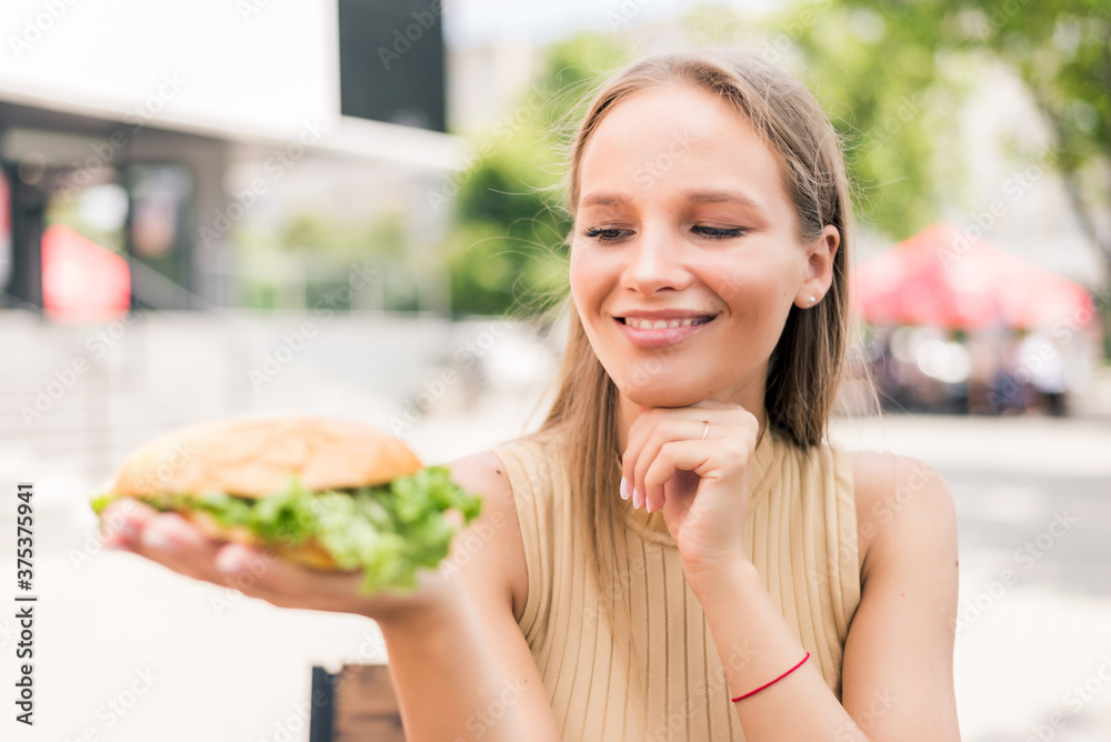 Young woman holding burger while sitting in outdoors fast food Young woman holding burger while sitting in outdoors fast food