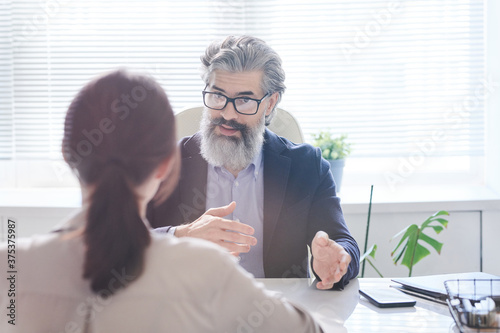 Modern mature man with beard on face discussing business project plan with woman sitting in front him photo