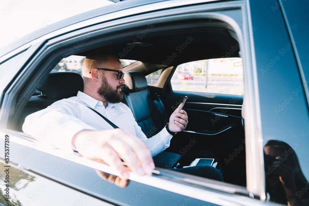 Successful Caucasian male financial director of corporate company reading received email with business information about contract connecting internet roaming during business trip in executive car