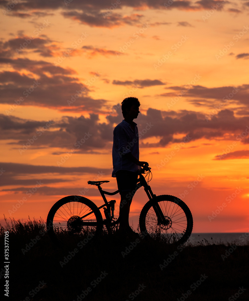 Obraz premium Silhouette of a young man with a Bicycle against the background of a sunset.