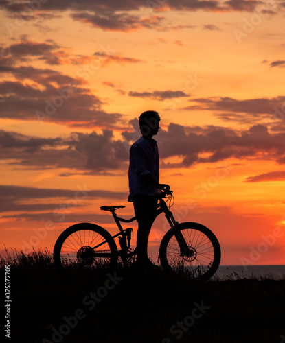 Silhouette of a young man with a Bicycle against the background of a sunset.