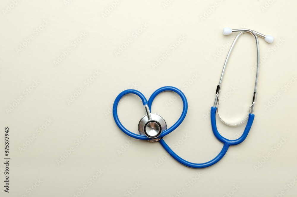 Top view of blue stethoscope in heart shape on the bright beige surface.Empty space Top view of blue stethoscope in heart shape on the bright beige surface.Empty space