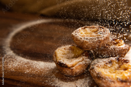 pastel di nata's getting sprinkled on a wooden board