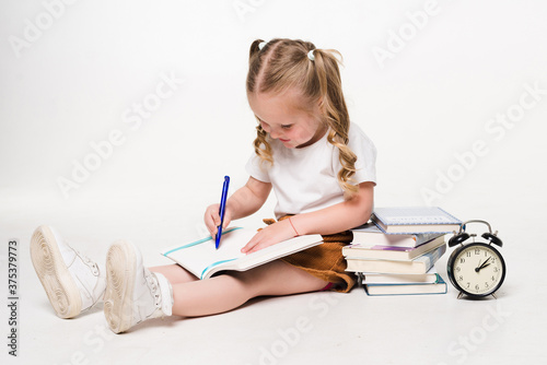 Little girl laying on the floor and drawing pictures in a notebook on white background
