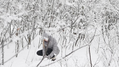 Attractive beautiful girl in the winter forest during a snowfall with a happy look admires nature, collects and throws snow.Sculpts and throws snowballs. She's happy Slow motion