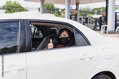 Coronavirus pandemic concept senior woman with protective mask thumb up sit in a car road trip travel.