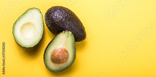 Two Haas avocado fruits on yellow colored  background. Slice avocado