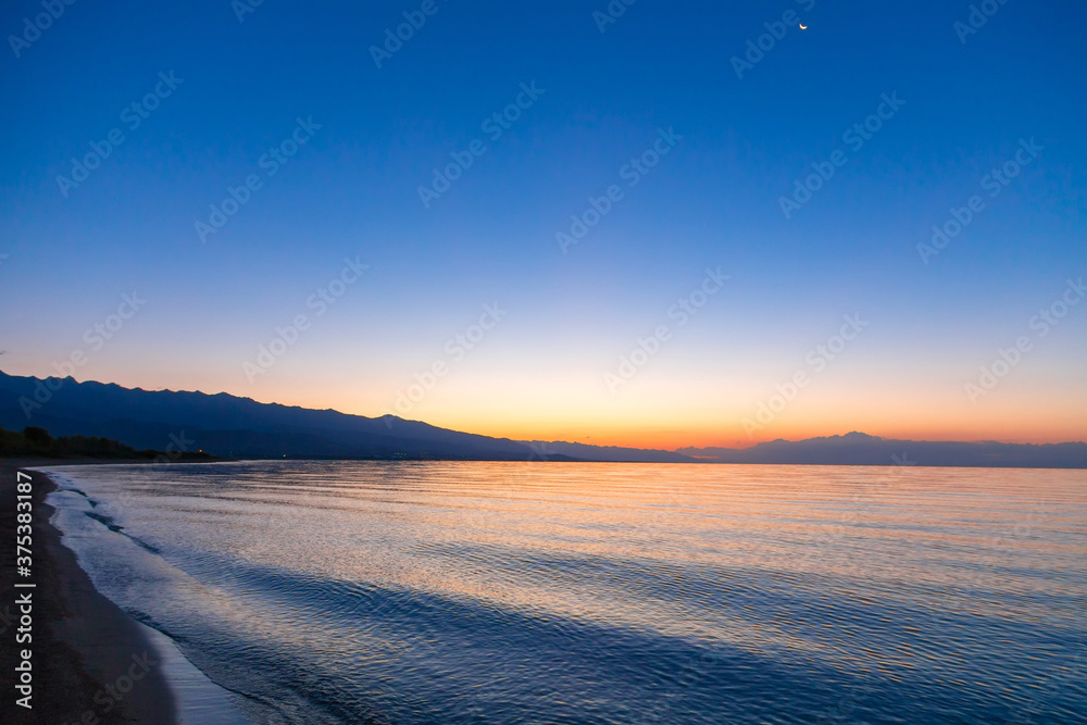 Dawn of the sun at sea. The rising sun behind the mountains. Kyrgyzstan.