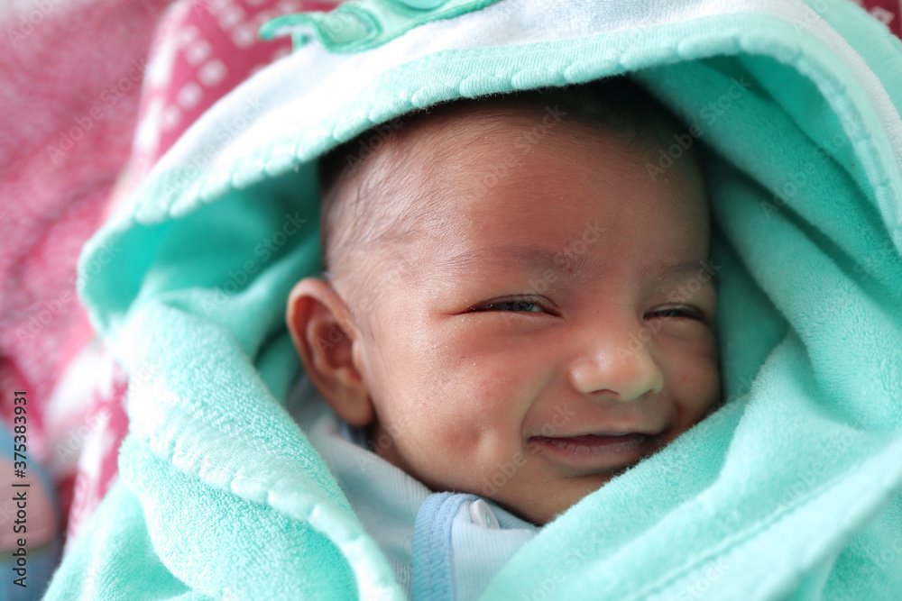 a smiling newborn baby with dimple in cheek wrapped in sea green colored towel with hood with eyes closed with selective focus on front eye a smiling newborn baby with dimple in cheek wrapped in sea green colored towel with hood with eyes closed with selective focus on front eye