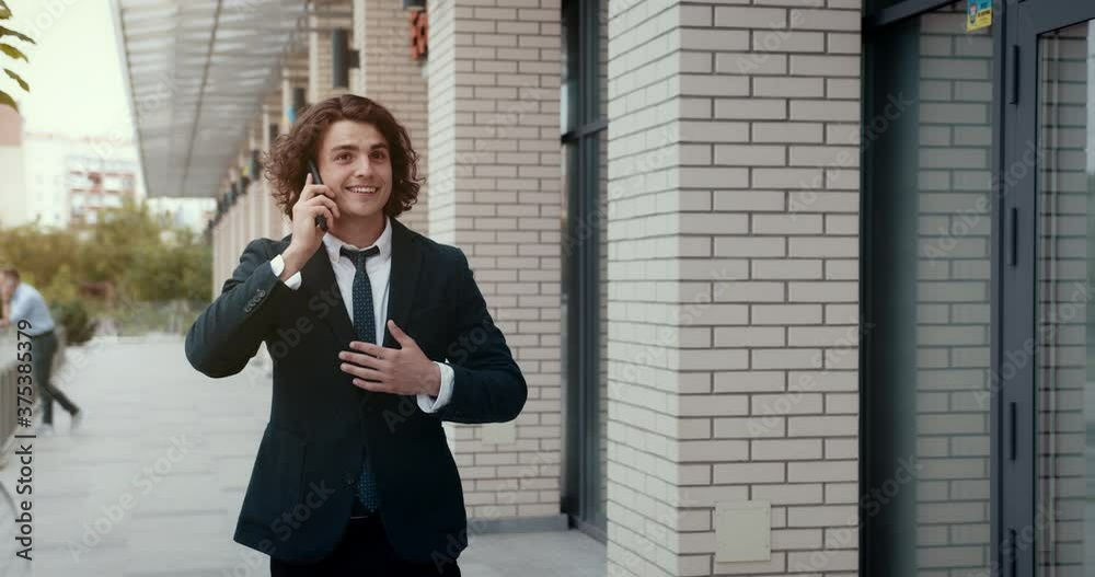 Confident smiling young businessman walking outdoors, talking on mobile phone, laughing, overwhelmed by pleasant conversation. Confident smiling young businessman walking outdoors, talking on mobile phone, laughing, overwhelmed by pleasant conversation.