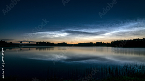 night landscape with white silver clouds over the lake, blurred foreground, charming cloud reflections in the lake water, summer night © ANDA