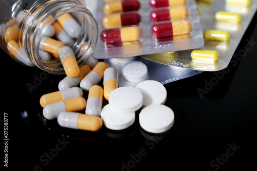 Pills on a dark glass table, variation of medication in capsules and tablets scattered from a bottle. Concept of pharmacy, antibiotics, vitamins photo