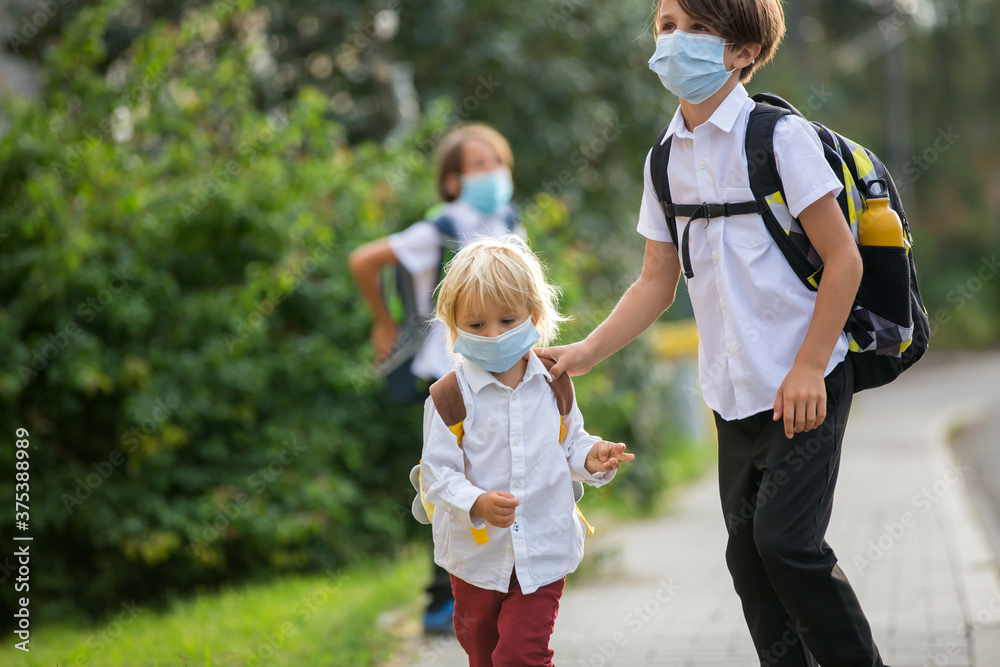 Fototapeta premium School children, boys, going back to school after the summer vacation, kids going to school wearing medical mask due to coronavirus