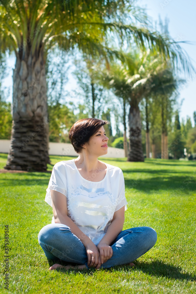 cute adult woman sits on the grass under palm trees. concept of active and happy retirement elderly citizen outdoors.