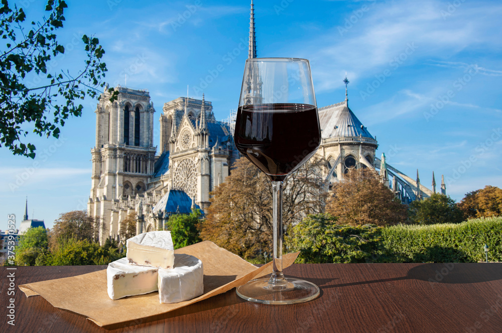 Glass of red wine with brie cheese against Notre Dame de Paris or Notre-Dame Cathedral in Paris, France. Romantic celebration.