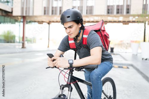 Latin Delivery Man Using Mobile Phone On Bicycle