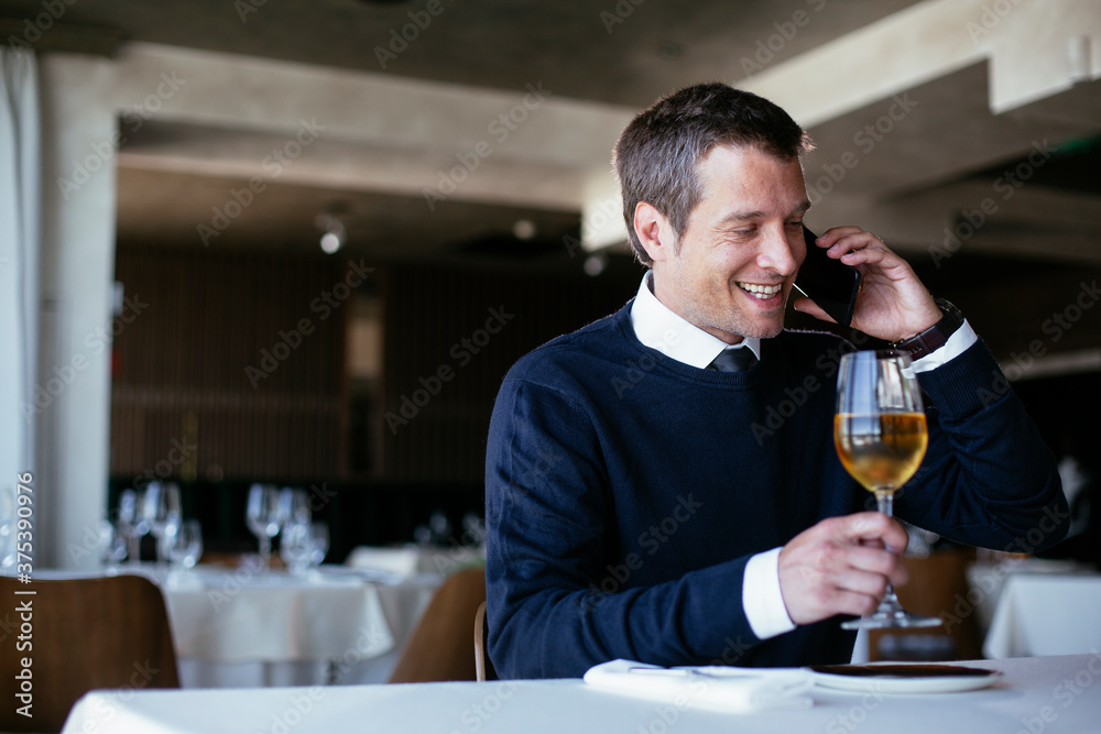 Handsome businessman dressed in the suit drinking wine. Businessman talking to the phone..