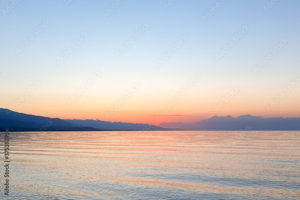 Dawn of the sun at sea. The rising sun behind the mountains. Kyrgyzstan.